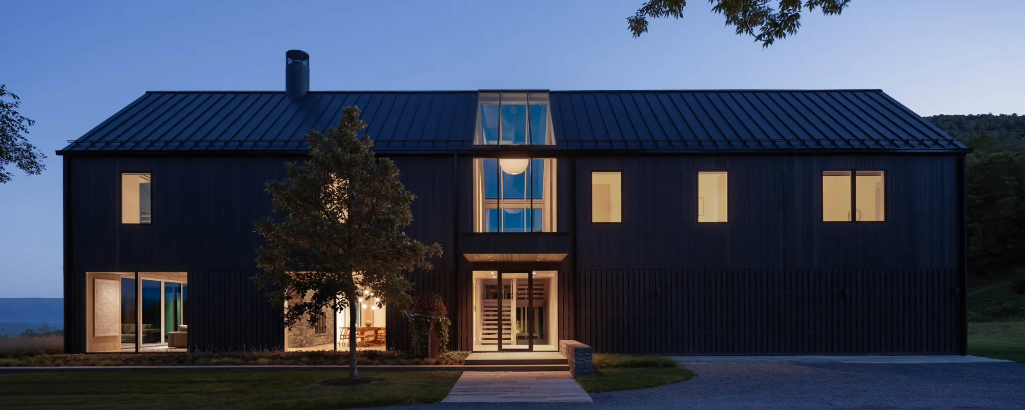 A dark-sided Vermont home at dusk with warm light in every window