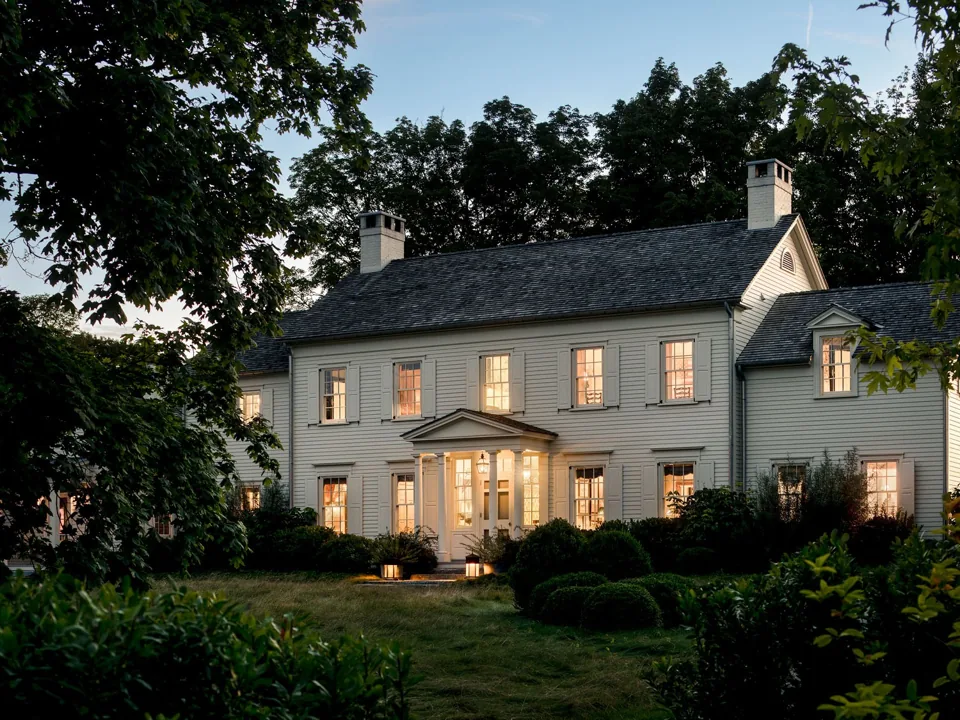 Lake House at dusk, its classic facade lit from within among old trees